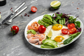 Keto breakfast with salmon, boiled shrimps, prawns, fried eggs, fresh salad, tomatoes, cucumbers, and avocado. Concept of healthy eating