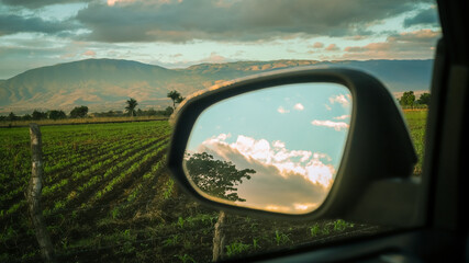 view of the countryside landscape from the rear view mirror of a vehicle at sunrise
