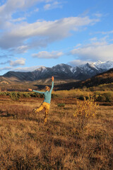 A happy hiker runs across the field against the backdrop of mountains covered with snow. Russian mountain hike.