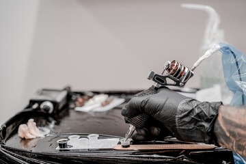 Hand of professional artist with tattoo machine, petroleum jelly and plastic cups with inks, close...