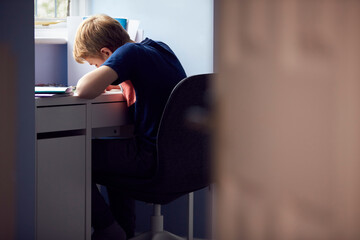 View Through Door Of Boy Sitting At Desk Home-Schooling