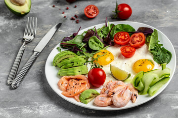 Ketogenic Low Carbohydrate Breakfast salmon, boiled shrimps, prawns, fried eggs, fresh salad, tomatoes, cucumbers and avocado. top view