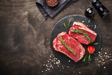 Two raw steak New York  with rosemary and spices on a piece of parchment paper on old dark stone background. Top view. Mock up.