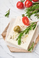 Cheese feta with rosemary, herbs, cherry tomatoes, olives and olive oil on wooden cutting board on white old wooden background. Traditional Greek homemade cheese. Selective focus.