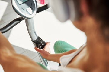 Closeup of young woman adjusting speed on stationary bike during morning cardio workout