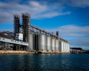 Obraz premium Grain storage tanks in the port next to the sea with a blue sky