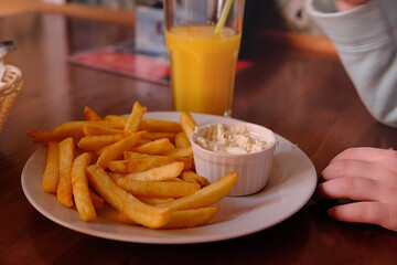 Little girl sitting at table and eating French fries and drinking orange juice in cafe