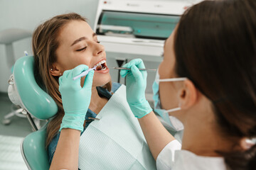 Woman sitting in medical chair while dentist fixing her teeth