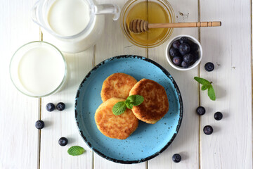 Delicious breakfast: sweet cottage cheese with honey on a blue plate on a white table. Top view