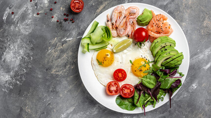 Ketobreakfast salmon, boiled shrimps, prawns, fried eggs, fresh salad, tomatoes, cucumbers and avocado. Concept of healthy eating. menu recipe place for text, top view