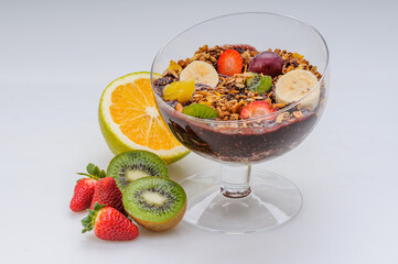 Acai with granola and fruits like strawberry, grape, banana, papaya, orange, kiwi in a glass bowl on a white background. Healthy food.