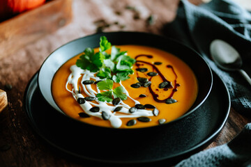 Vegetarian, homemade pumpkin cream soup in a bowl on wooden table. 
