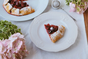 Delicious freshly baked vegan strawberry and cherry galette on white rustic tableclothd with hydrangea flowers. Sweet food, summer dessert.
