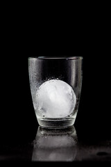 ice ball inside cocktail glass on a reflective black table.