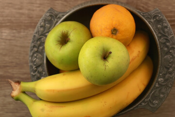 Antique bowl with bananas, apples and lemons on wooden table. Top view.