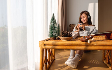 A beautiful young asian woman enjoy drinking coffee and listening to music with headphone at home