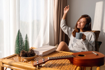 A beautiful young asian woman enjoy drinking coffee and listening to music with headphone at home