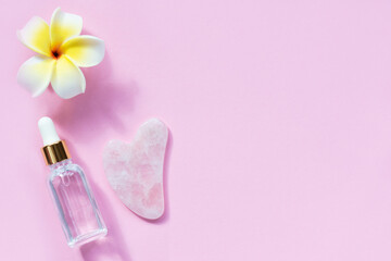 Gua sha scraper with oil and frangipani flower on a pink background. Horizontal orientation, copy space, top view.