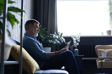 Mature handsome man websurfing on tablet at home.