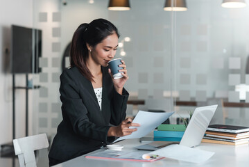 Asian businesswoman sitting looking at document with drinking coffee at the office.