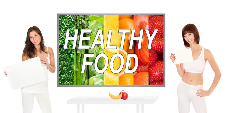 Two beautiful young women wearing white sportswear and holding blank posters in front of a colorful photo with fruits and vegetables, healthy food is written on the image, isolated on white background