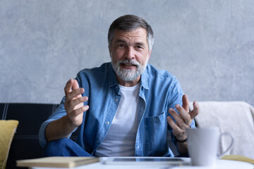 Happy senior retired man blogger looking at camera recording vlog, webcamera view portrait