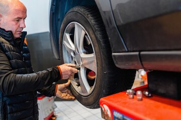 Mechanic in a car repair shop loosening the wheel nuts of a vehicle.