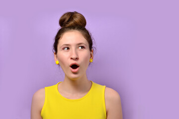 Photo of a cute girl opening her mouth while singing and looking away in a yellow dress on a lilac bed background. Cute girl looks away, mouth open. Portrait of a young girl in a bright yellow dress