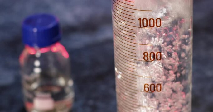 Water is poured into a large measuring chemical cylinder up to the level of two liters, a lot of air bubbles are formed in the water. The camera moves upward along the filling of the vessel.