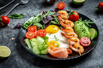 Healthy breakfast with salmon, grilled shrimps, prawns, fried eggs, fresh salad, tomatoes, cucumbers and avocado. keto diet. Top view