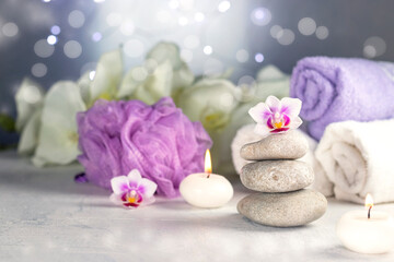 Fototapeta na wymiar massage stones, burning candles, rolled towels, flowers, abstract lights. Spa resort therapy composition
