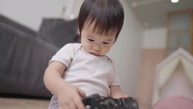 A little cute baby girl intently looking at camera's screen, adorable infant randomly pressing button and sitting in front of living room's sofa , modern nursery in braking time on background 