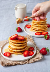 Stack of pancakes with strawberry and pouring golden honey on grey background 