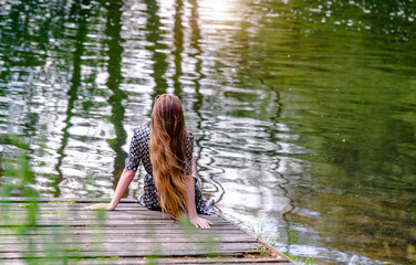 The girl is sitting on a wooden platform near the lake