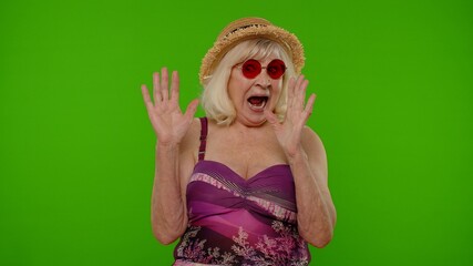 Scared senior woman tourist stretching out hands, stop gesture to hide from fear, looking terrified afraid, panic attack on chroma key. Travel, summer holiday vacation. Elderly grandmother in swimsuit