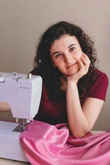 Happy attractive young woman seamstress sitting and sews on sewing machine in studio