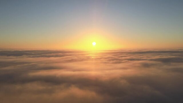 Beautiful cinematic shot flying above clouds looking at the sun setting or rising on the horizon as the clouds move and eventually cover the sun