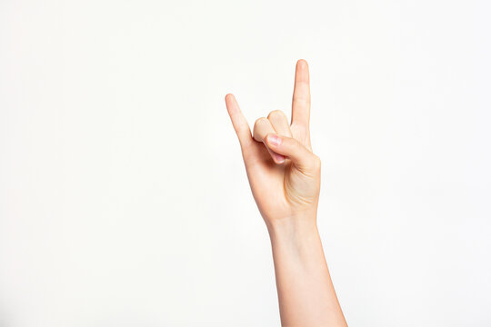 Woman's hand gesturing rock and roll, heavy metal, devil horns gesture or I love you on light grey background
