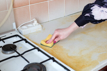 Woman wiping dirty yellow greasy table and gas stove.