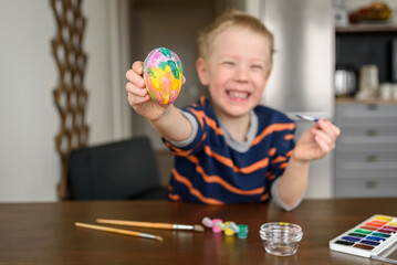 Fototapeta premium Happy smiling Boy coloring Easter egg at home with acrylic paint. Little artist, hobby
