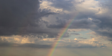 Naklejka na ściany i meble rainbow on dramatic dark sky with rays and white clouds