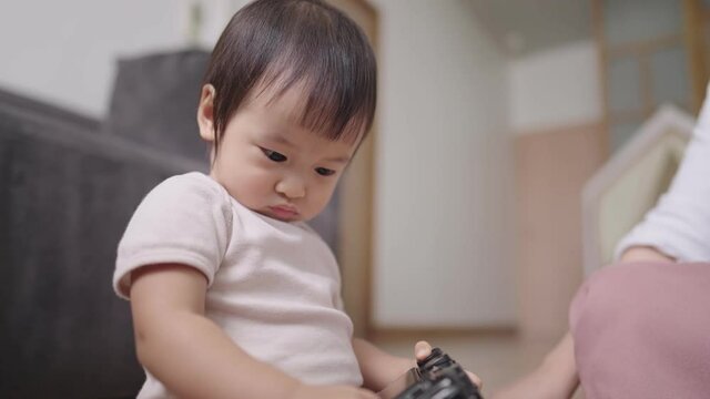 Cute smart little asian baby girl tries to tamper a camera shield, a curious toddler intently learn how to open camera screen, satisficed imagination, education and future careers in childhood
