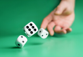 Hand throws dice on a green background with selective focus.
