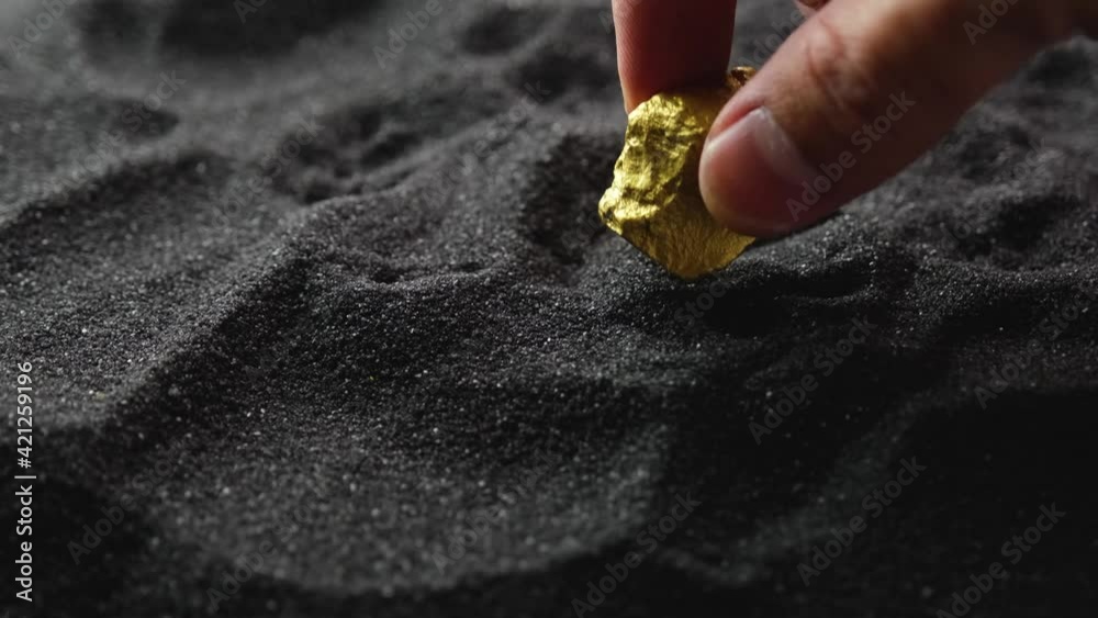 Wall mural man's hand is considering holding gold ore from mine on a black sand background.