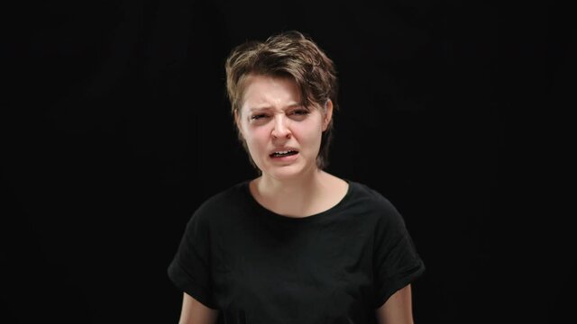 Furious young woman with hand on mouth looking at camera and screaming. Portrait of angry Caucasian stressed lady posing at black background. Fury and anger concept.