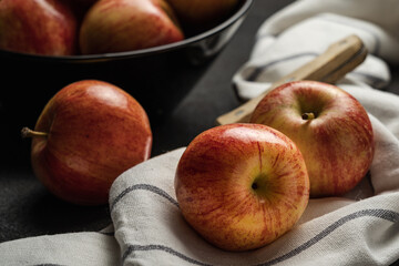Shiny apples on a cloth and in a bowl on a black table with a knife.