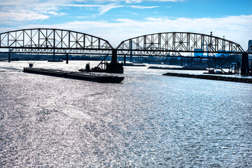 Towboat pushing dry bulk cargo barge under bridges up Mississippi River. Shipping grain corn during harvest season, cargo, food, raw, transportation, agriculture, agricultural, tow, marine, maritime