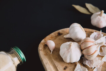 Garlic bulbs on wooden board on  black background, with dried garlic and bay leaves. Condiments and spices in kitchen.