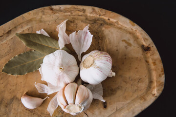 Garlic bulbs and bay leaves on wooden board, on black background. Garlic top view. Natural antibiotic. Cooking.