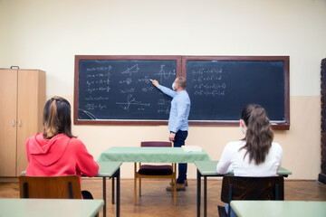 Students in protective face masks studying in classroom with teacher. Precautions in coronavirus pandemic